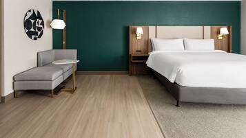 A hotel room with a bed, a gray sofa, a small table, and two wall-mounted lamps.