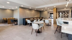 Un comedor moderno con mesas y sillas redondas, una zona de bar y un área de estar con bancos.