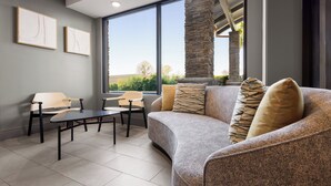 Una sala de estar moderna con un sofá gris, dos sillones, una mesa de centro y un ventanal con vistas a zonas verdes.