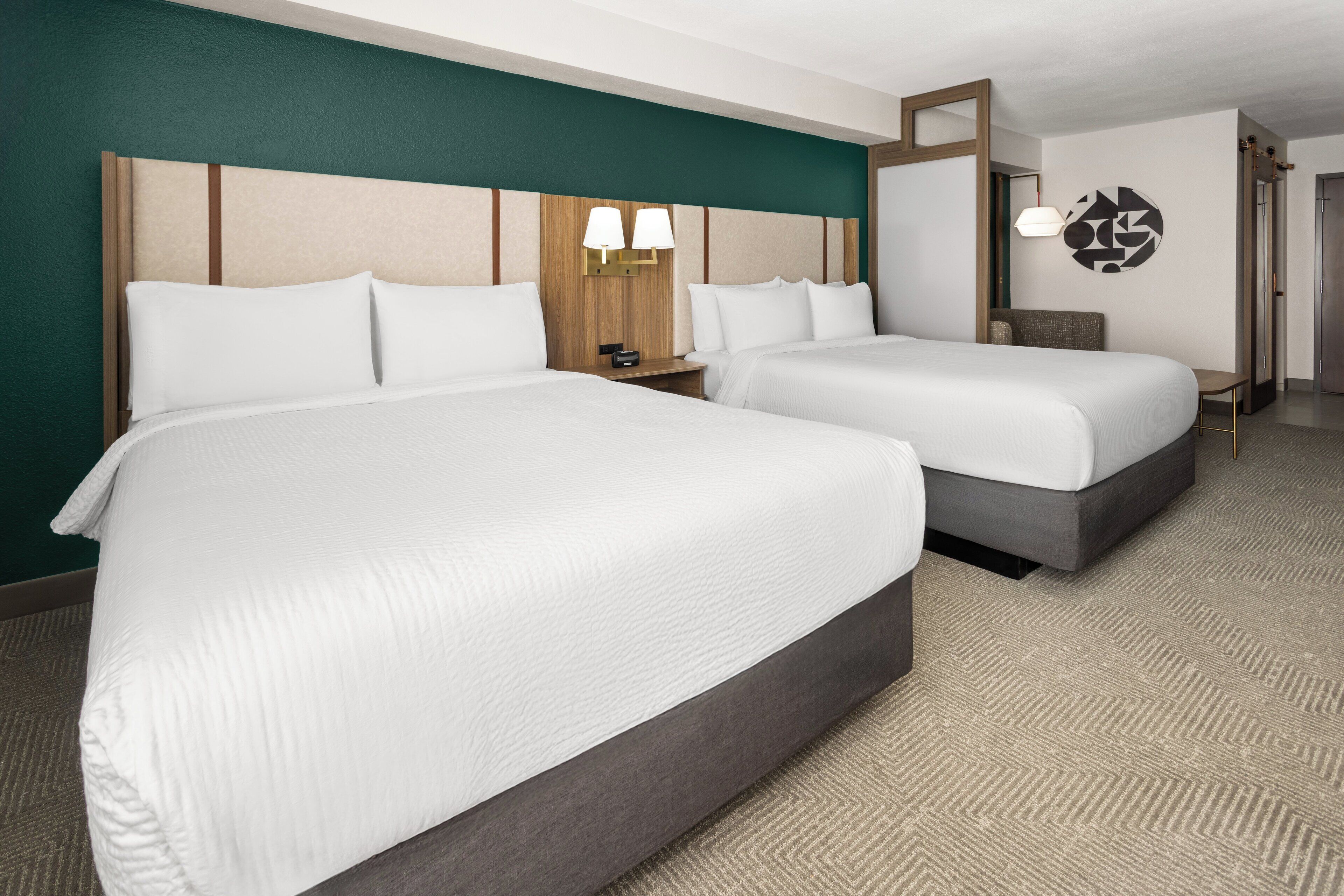 Una habitación de hotel con dos camas, un cabecero de madera, una lámpara de pared y suelo alfombrado.