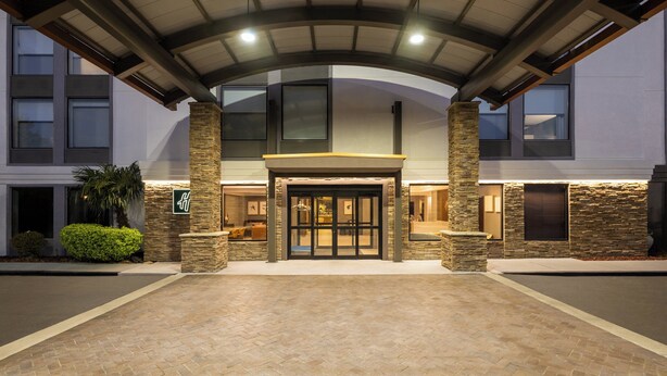Entrada de hotel con un corredor techado, pilares de piedra y puerta de vidrio.
