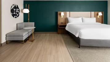 A hotel room with a bed, a gray sofa, a small table, and a wall art piece.
