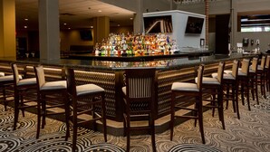 A bar area with a central counter displaying various bottles, surrounded by bar stools. - DoubleTree Suites by Hilton Hotel McAllen (McAllen)