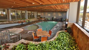 An indoor swimming pool area with wooden ceiling, seating around the pool, and a stone wall. - DoubleTree Suites by Hilton Hotel McAllen (McAllen)