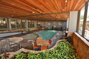 Un área de piscina interior con techo de madera, asientos alrededor de la piscina y una pared de piedra.