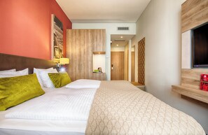 A hotel room with a large bed, a wooden headboard, a TV mounted on the wall, and a small shelf with items.