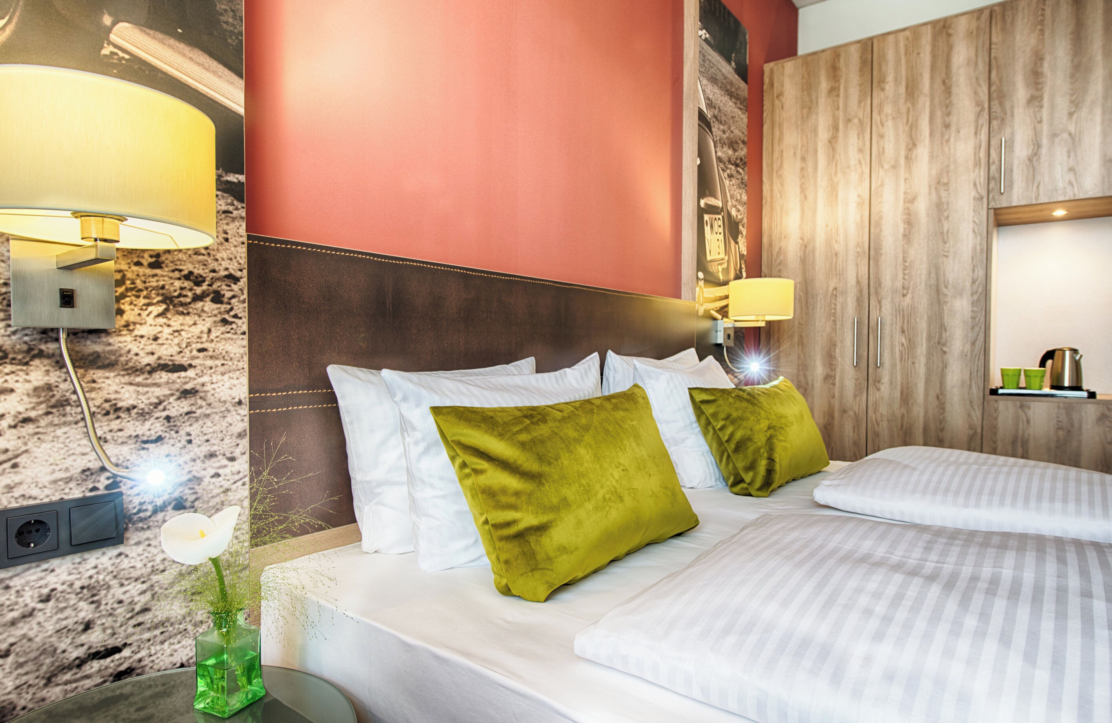 A hotel room with a marble wall, a wooden headboard, two beds with white bedding, green pillows, and two wall-mounted lamps.