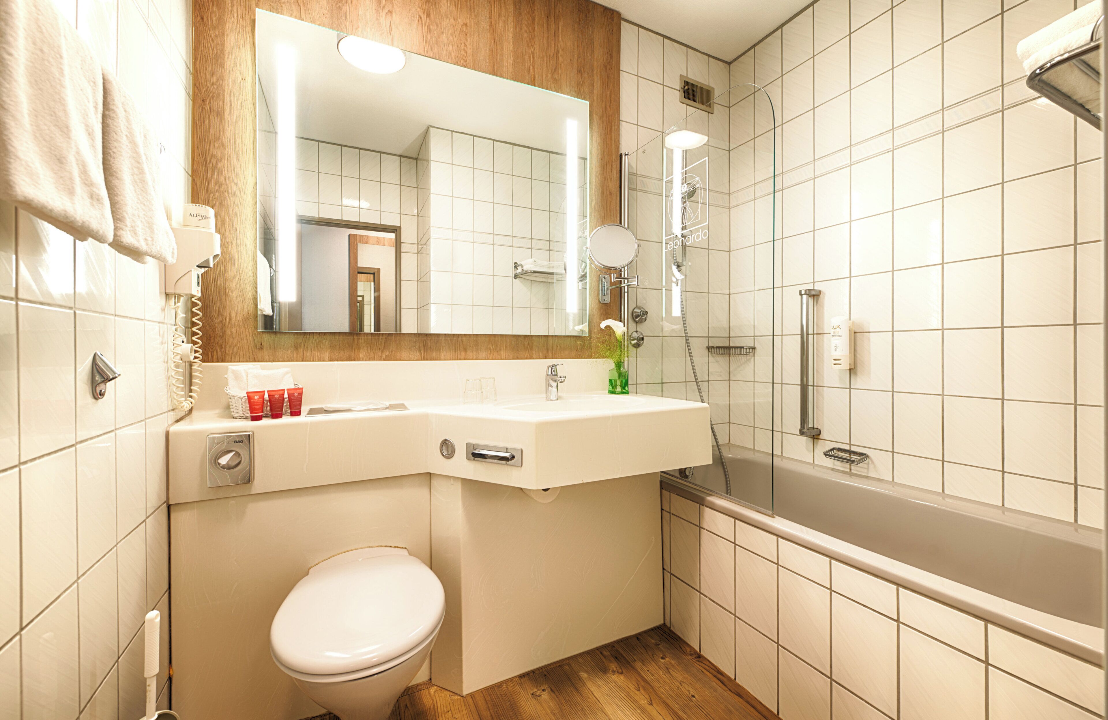 A modern bathroom with a toilet, sink, mirror, and shower.