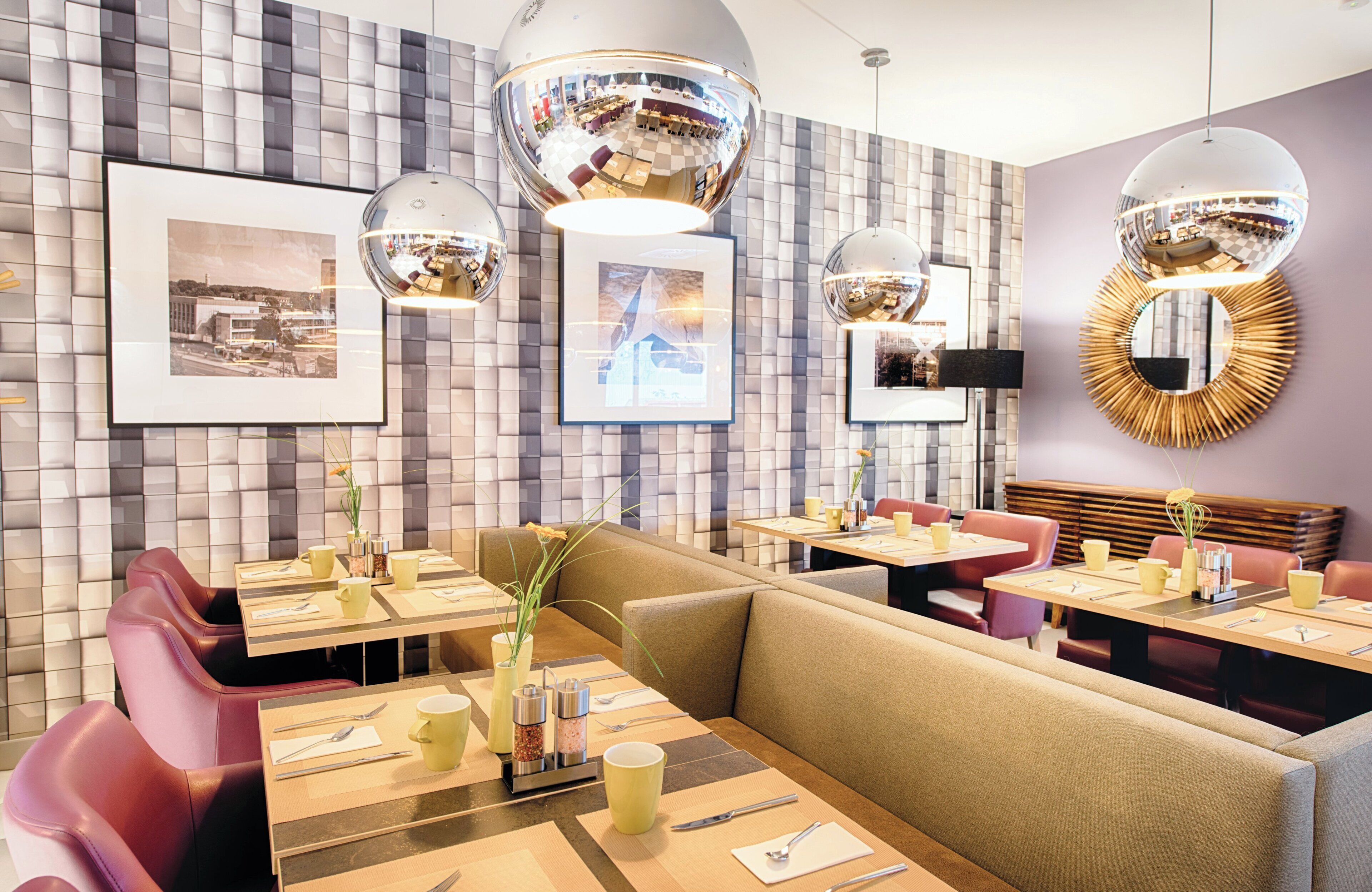 Ein modernes Restaurantambiente mit gepolsterten Sitzecken, rechteckigen Tischen und Pendelleuchten.