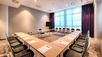 A conference room with a long table, chairs, a TV, and a large window with curtains.
