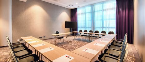 Un salón de conferencias con una larga mesa, sillas, un televisor y un amplio ventanal con cortinas.