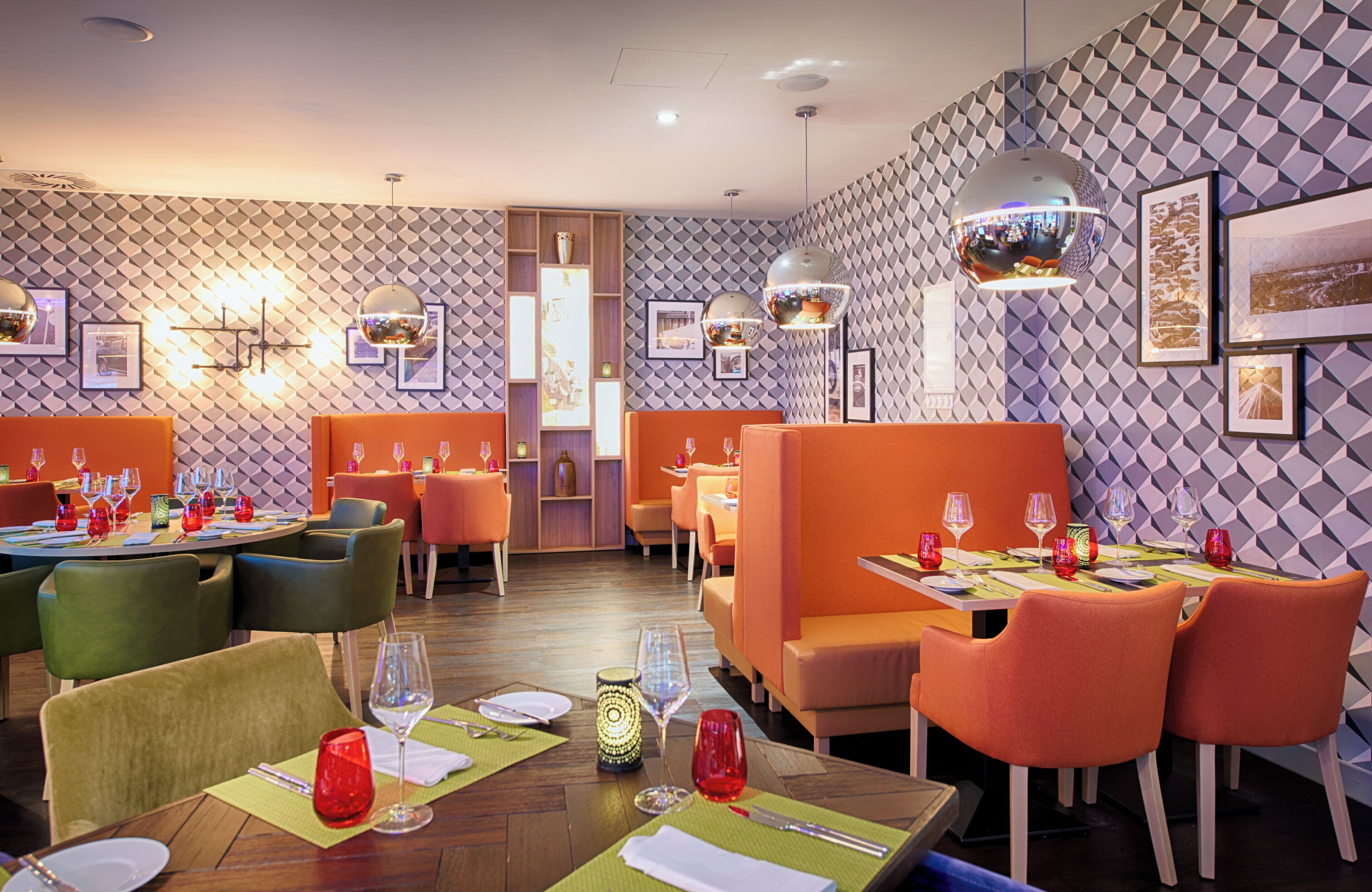 Un ristorante con parete a motivo geometrico, sedute arancioni e verdi, e diverse lampade a sospensione.