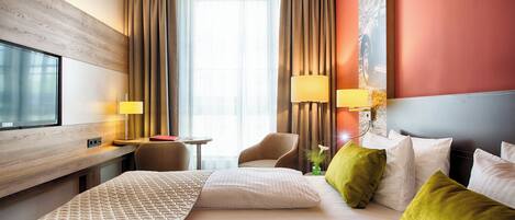Habitación de hotel con una cama grande, dos mesitas de noche, un escritorio, una silla, un televisor y una ventana con cortinas.