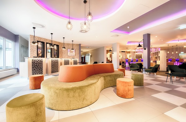 A modern lobby with a curved seating area, a reception desk, and a bar area with seating. - Leonardo Hotel Wolfsburg City Center (Wolfsburg)