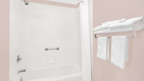 Une salle de bain avec une baignoire blanche, une pomme de douche et un porte-serviettes avec des serviettes pliées.
