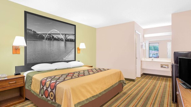 Une chambre d’hôtel avec un lit, une télévision, un bureau et une salle de bain, visibles à travers une porte ouverte.