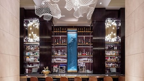 A bar area with a long counter, multiple shelves of bottles, and a large illuminated screen. - Hotel Crescent Court (Dallas)