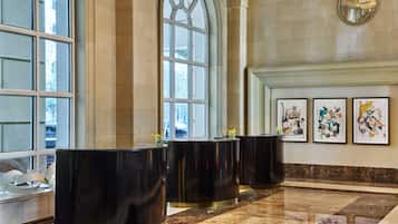 Um hall de entrada com piso de mármore, grandes janelas e três balcões de recepção pretos.