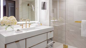 A modern bathroom with a large mirror, white sink, gold fixtures, and a glass shower enclosure.