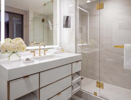 A modern bathroom with a large mirror, white sink, gold fixtures, and a glass shower enclosure.