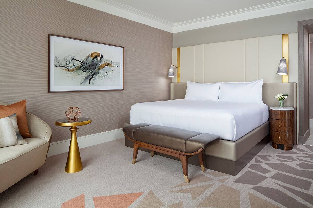 Ein modernes Hotelzimmer mit einem großen Bett, einem kleinen Nachttisch, einer Bank und einem Gemälde an der Wand.