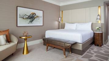 A modern hotel room with a large bed, a small side table, a bench, and a painting on the wall.
