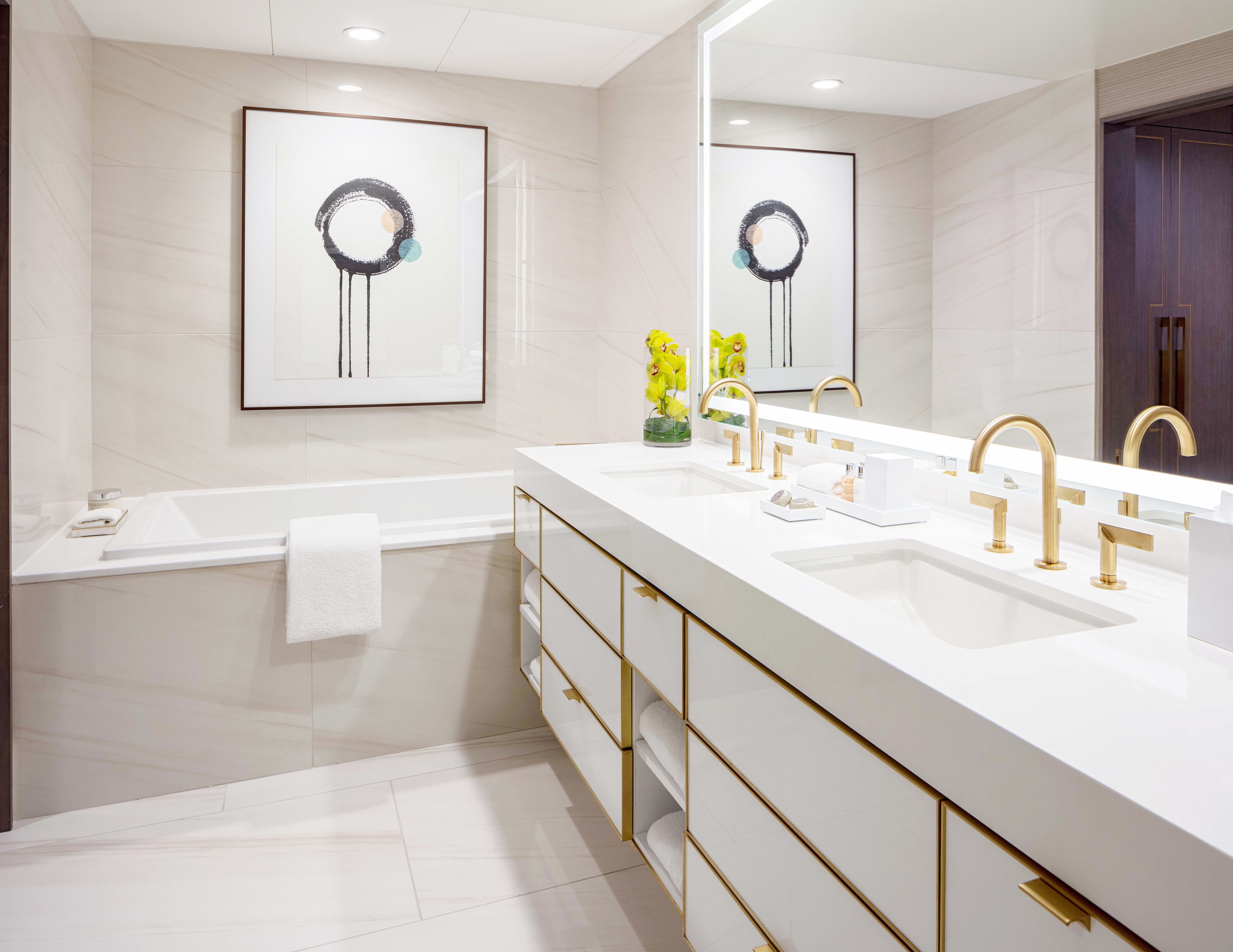 A modern bathroom with a white vanity, gold faucets, and a large mirror.