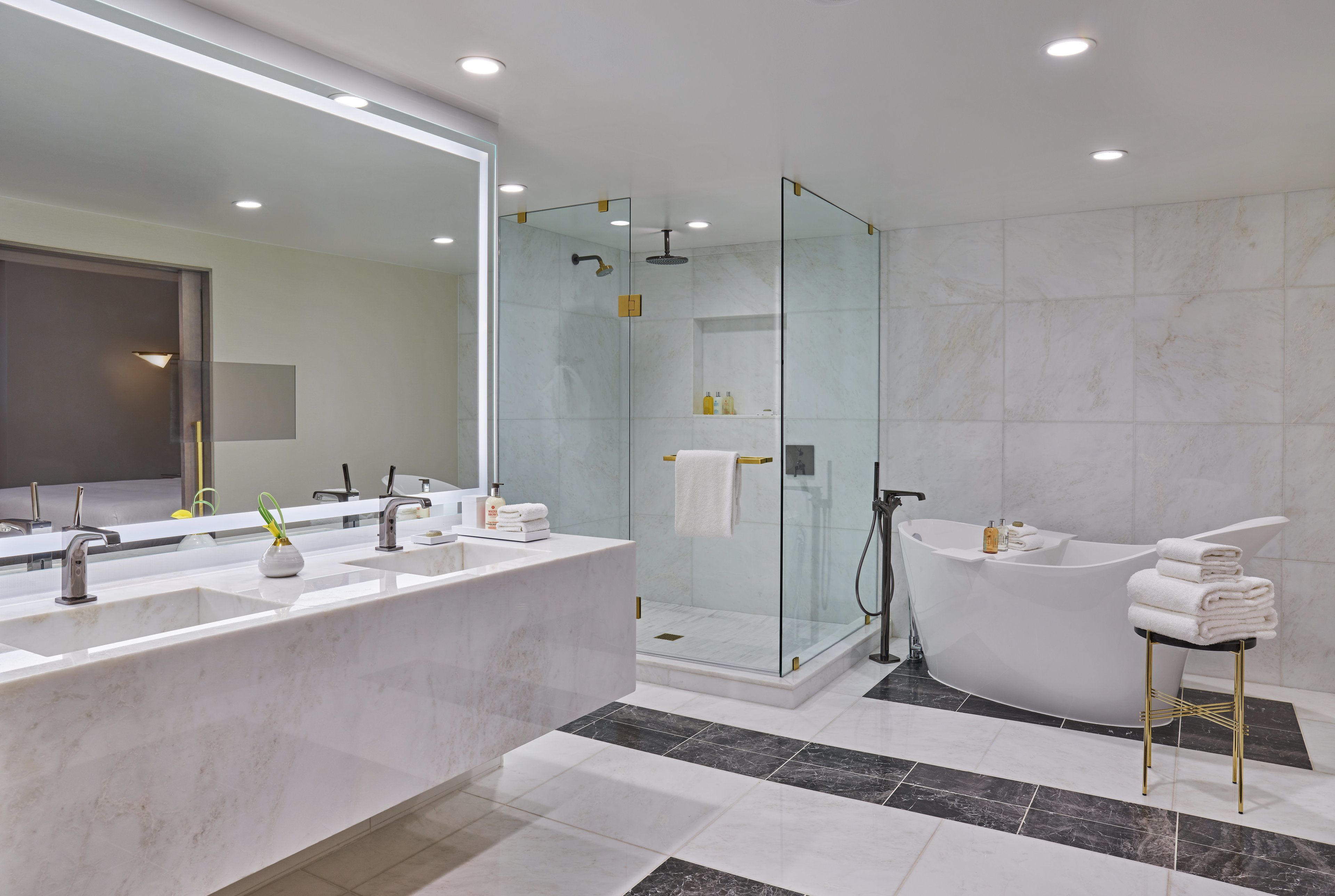 Un baño moderno con un espejo grande, dos lavamanos, ducha envuelta en cristal y una bañera independiente.
