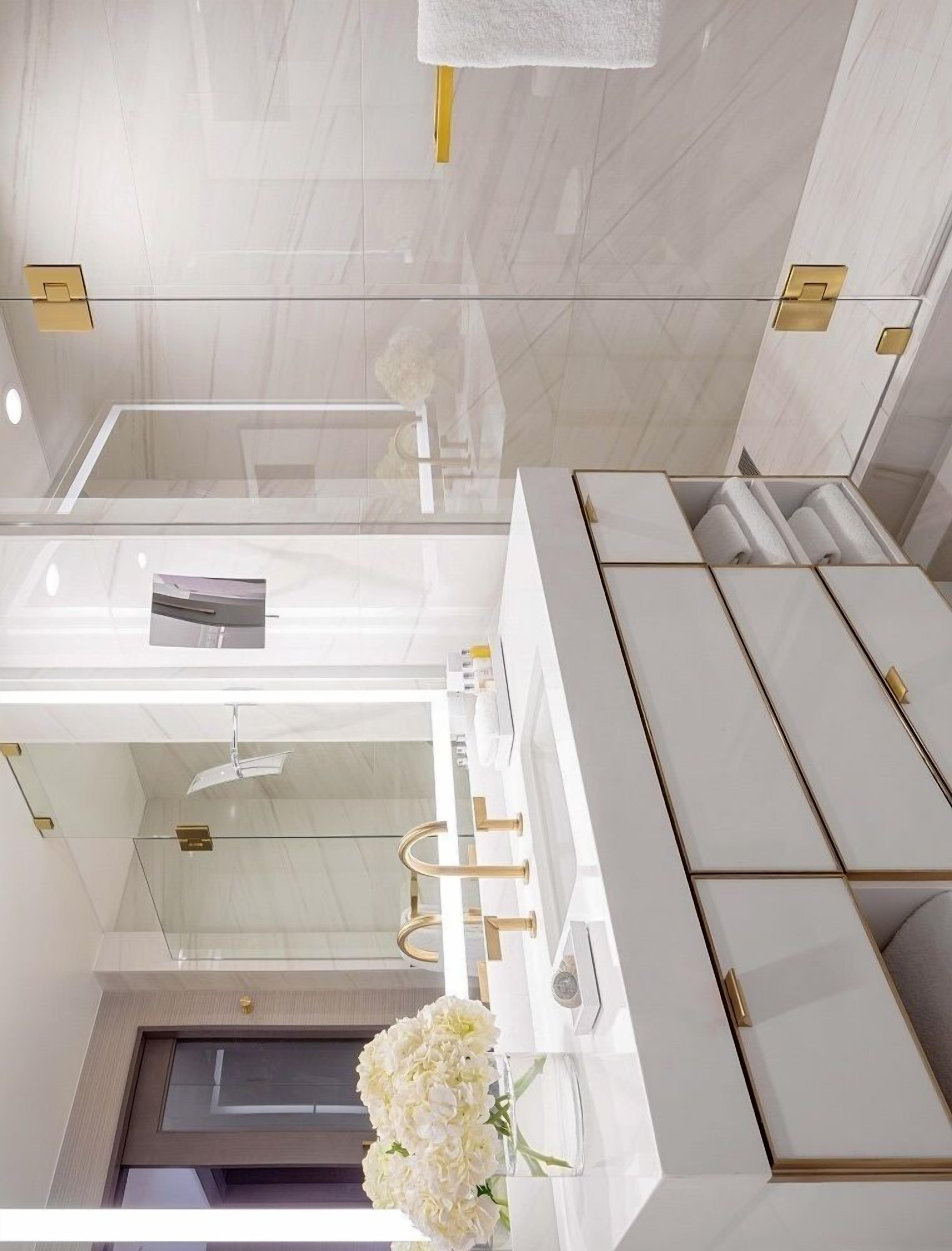 Une salle de bain moderne avec une douche à parois de verre, un meuble-lavabo blanc agrémenté de touches dorées et un arrangement floral.