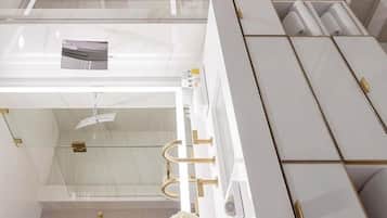 Une salle de bain moderne avec une douche à parois de verre, un meuble-lavabo blanc agrémenté de touches dorées et un arrangement floral.