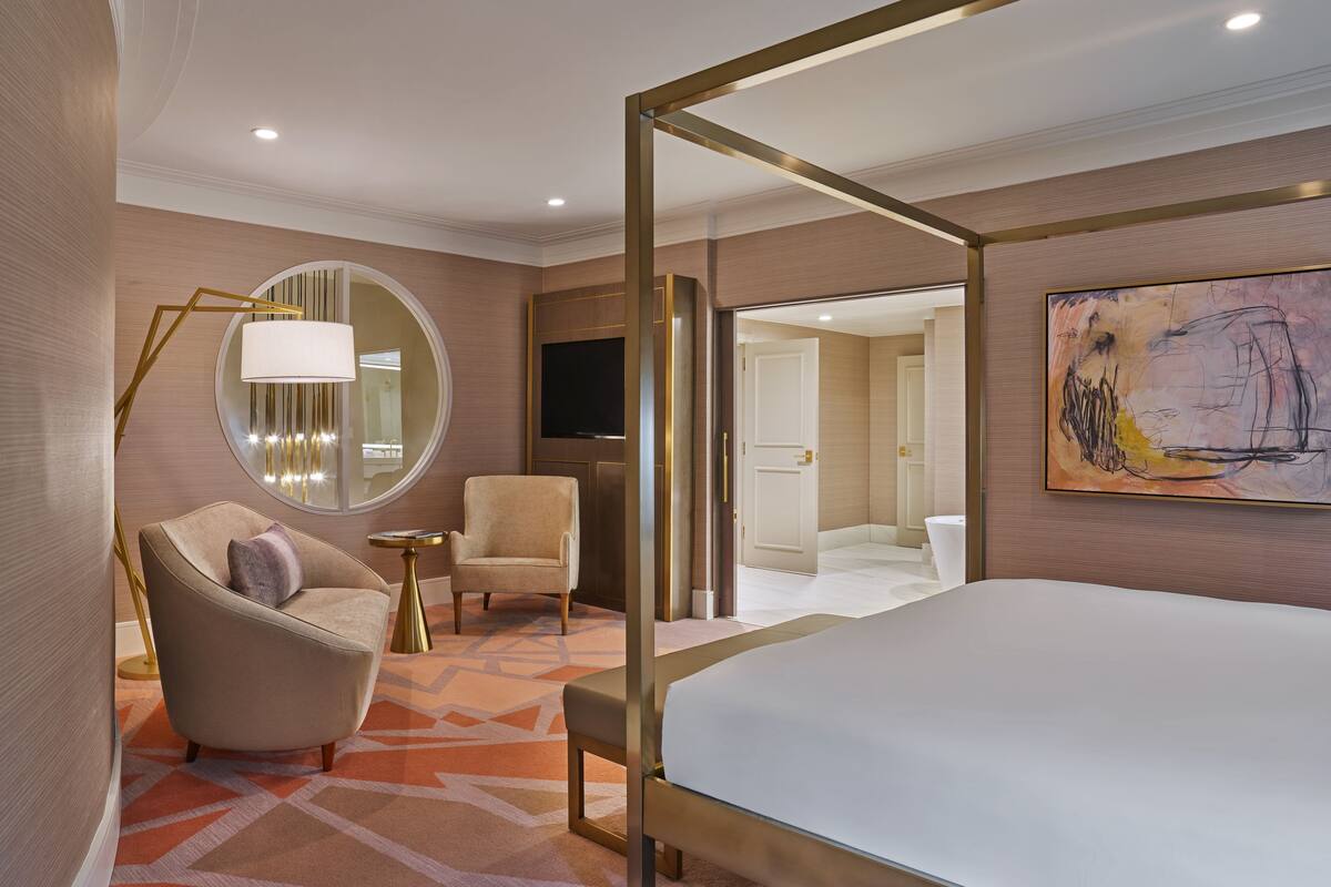 Ein modernes Hotelzimmer mit einem großen Bett, einem runden Spiegel, einem Sessel, einem kleinen Tisch und einem Fernseher.