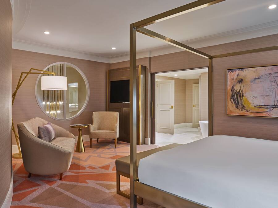 Una habitación de hotel moderna con una cama grande, un espejo redondo, una silla, una mesita y un televisor.