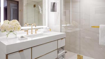 A modern bathroom with a white vanity, gold fixtures, and a glass shower enclosure.