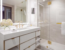 A modern bathroom with a white vanity, gold fixtures, and a glass shower enclosure.