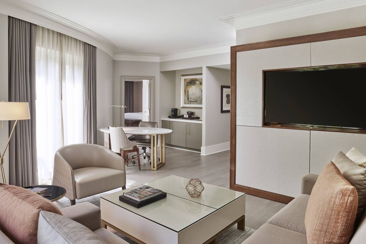 Ein modernes Hotelzimmer mit Wohnbereich, Esstisch, Küche und einem großen Fernseher.