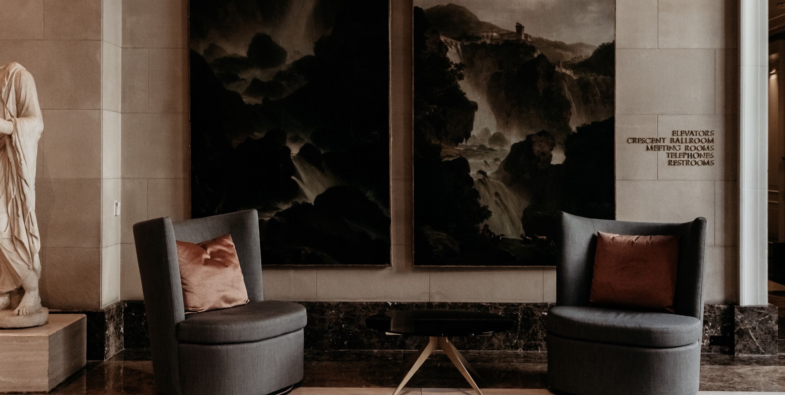 A lobby with two armchairs, a marble floor, and a large painting of a mountainous landscape.