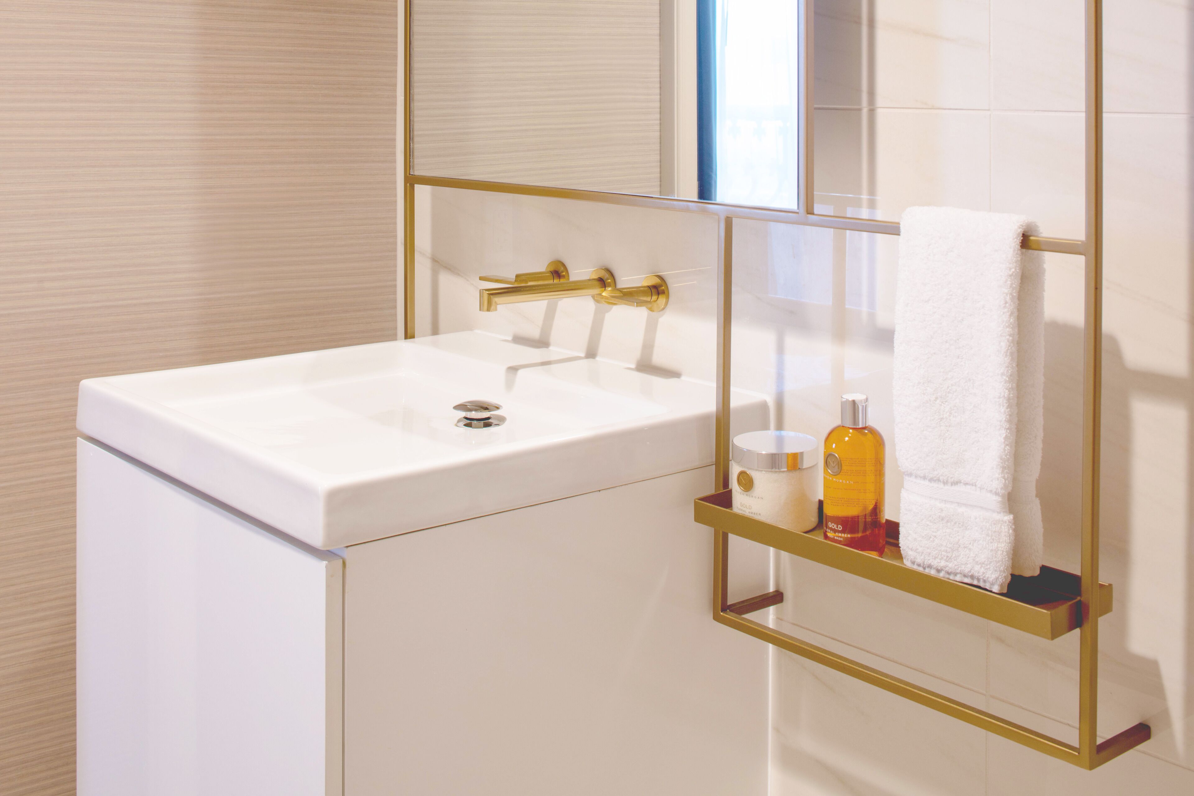 A bathroom with a white sink, gold faucet, and a towel hanging on a gold towel rack.