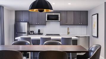 A modern kitchen with dark cabinetry, a central island, and a dining area with a wooden table and chairs.