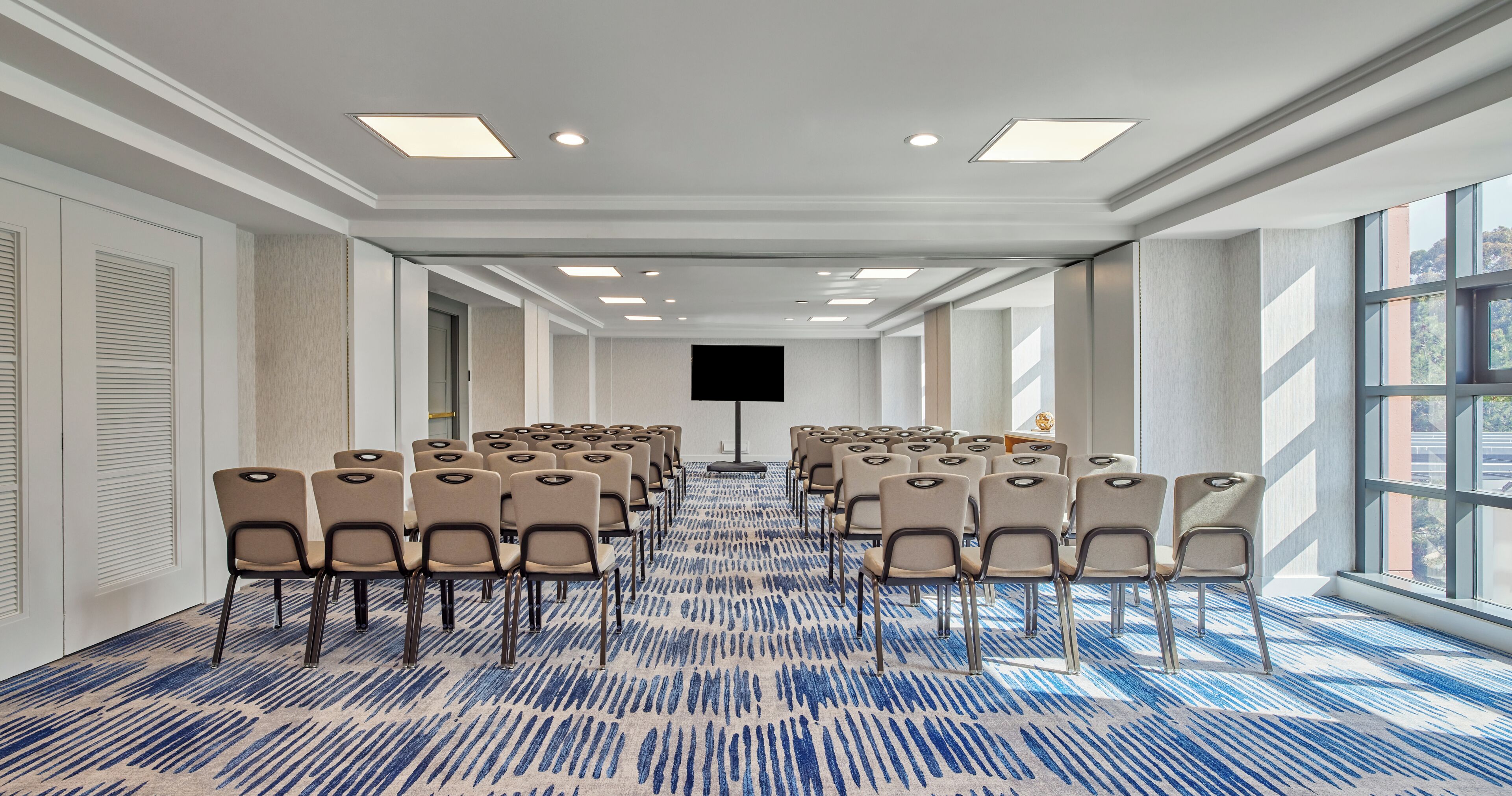 A conference room with rows of chairs, a large screen, and a patterned carpet.