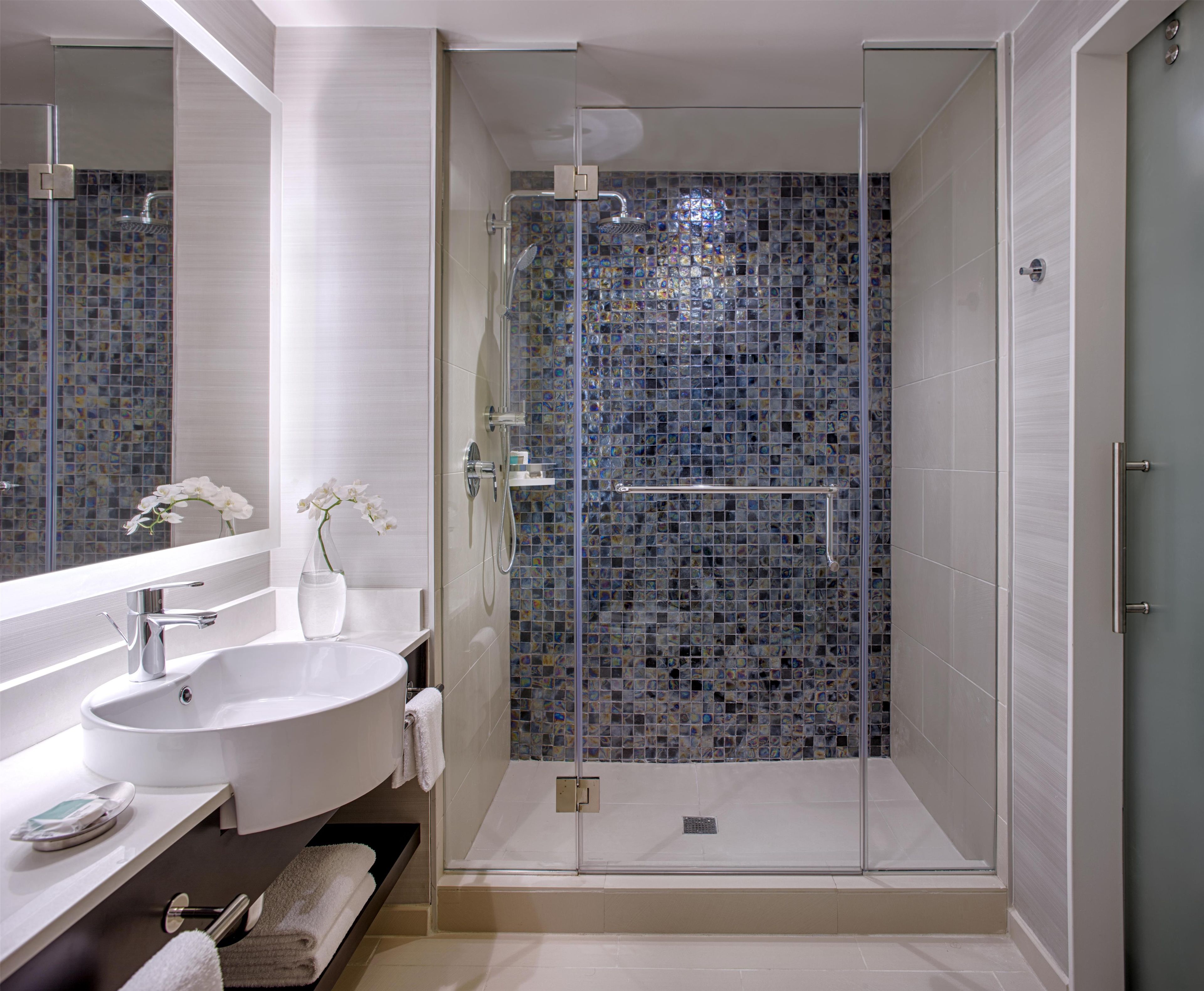 Ein modernes Badezimmer mit einer gläsernen Dusche, einem weißen Waschbecken und einem Spiegel.