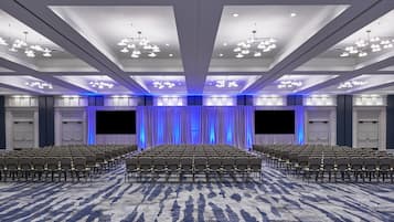 Un salón de conferencias con filas de sillas, un escenario con cortinas y una gran pantalla.
