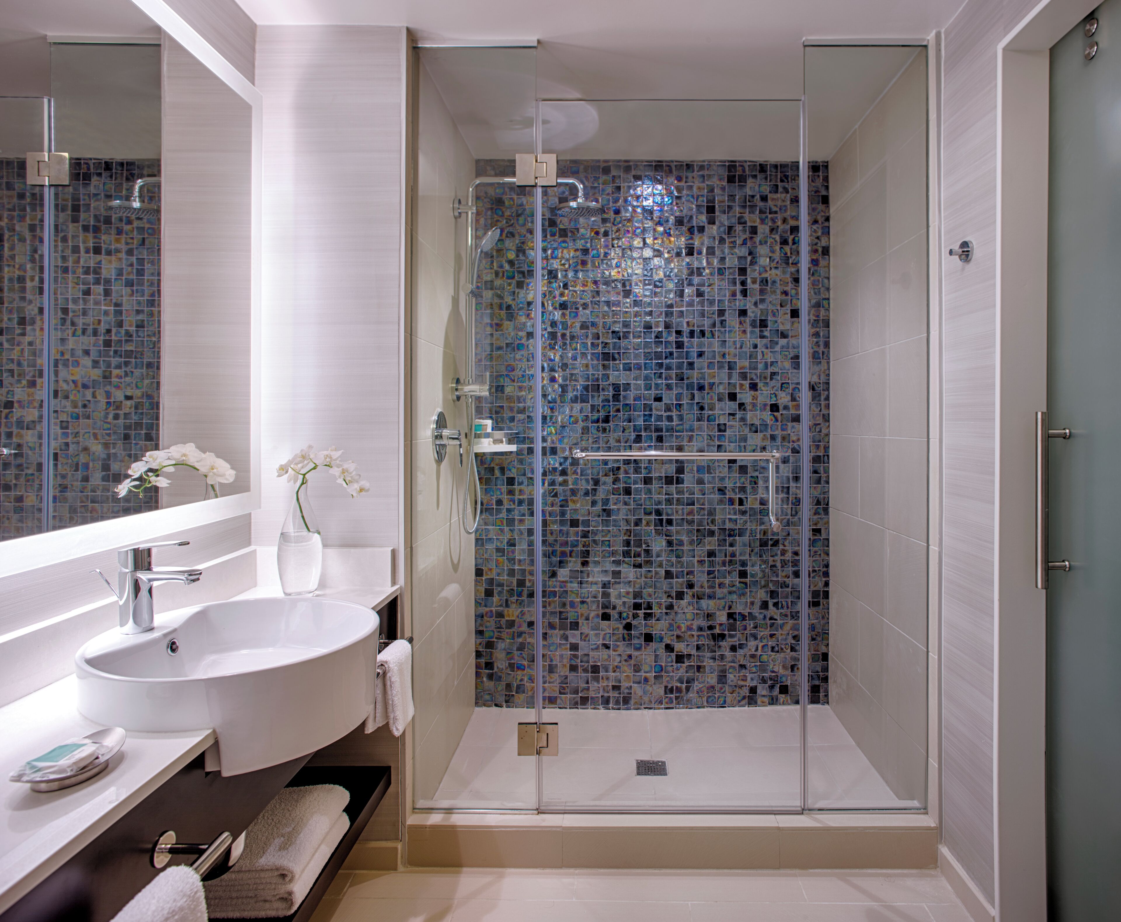 A modern bathroom with a glass-enclosed shower, a white sink, and a mirror.