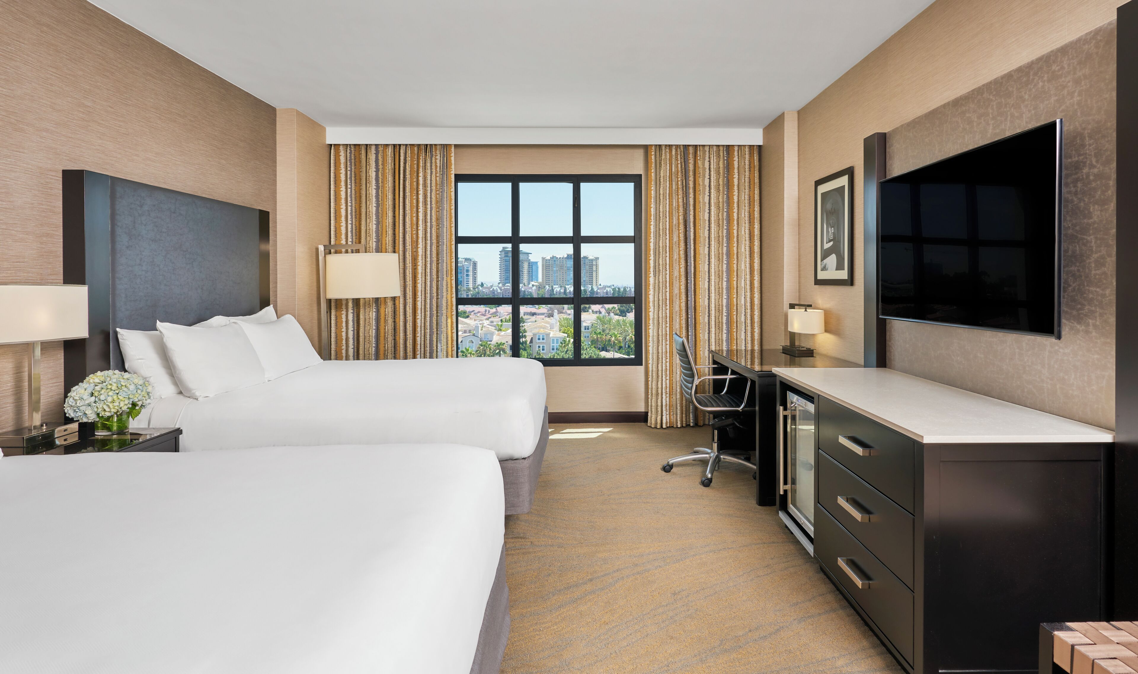 Une chambre d’hôtel avec deux lits, un bureau, une télévision et une fenêtre donnant sur la ville.