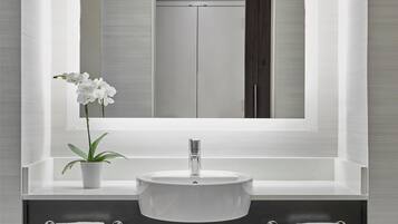 A bathroom with a white sink, a mirror, a potted plant, and two towel racks.