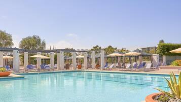 A swimming pool with sun loungers and umbrellas, surrounded by a pergola structure.