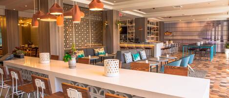 A modern bar area with a long counter, multiple seating options, and pendant lighting.