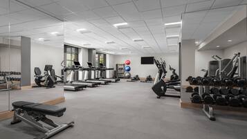 A gym with exercise equipment, mirrors, and a wall-mounted TV.