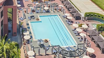 A rooftop swimming pool with sun loungers and umbrellas, surrounded by a landscaped area with trees and a tennis court.