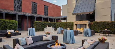 An outdoor seating area with sofas, a fire pit, and tables covered with blue tablecloths.