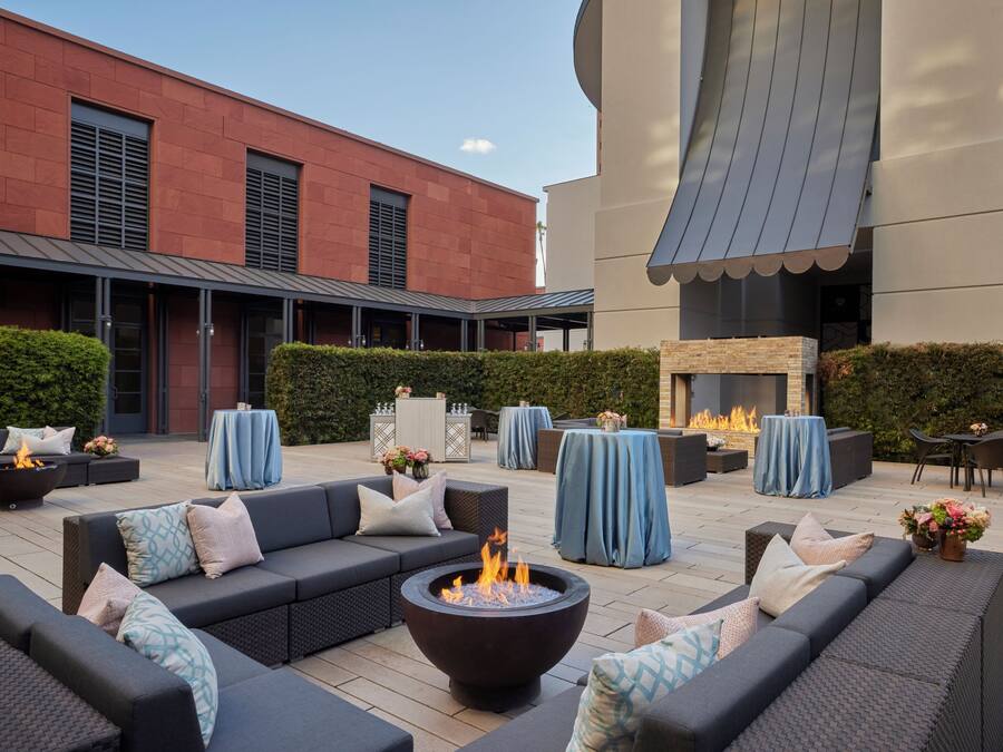 An outdoor seating area with sofas, a fire pit, and tables covered with blue tablecloths.